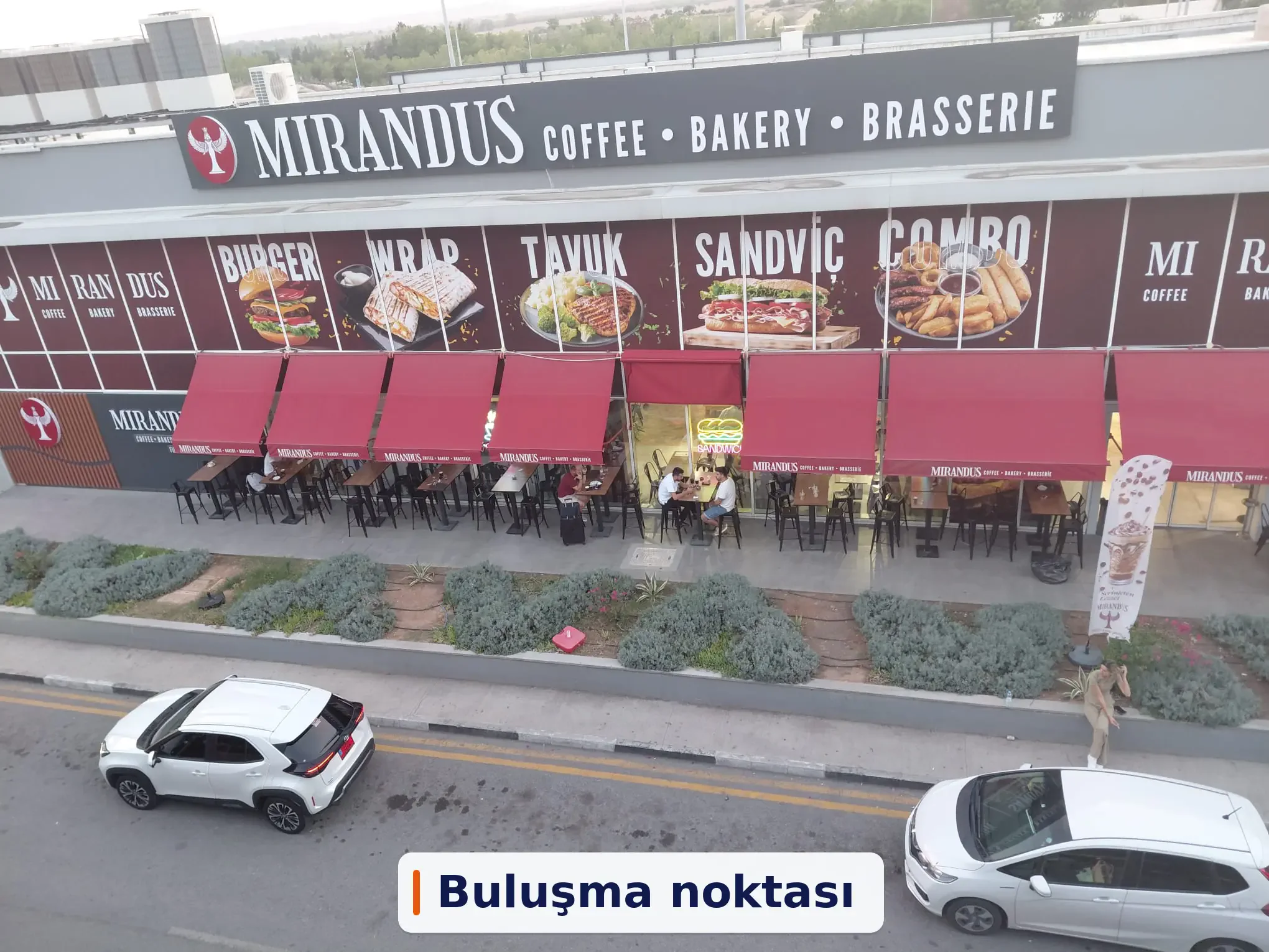 Terminal dışındaki Mirandus Cafe cephesi, tabelası, kırmızı tenteleri ve dış oturma alanı