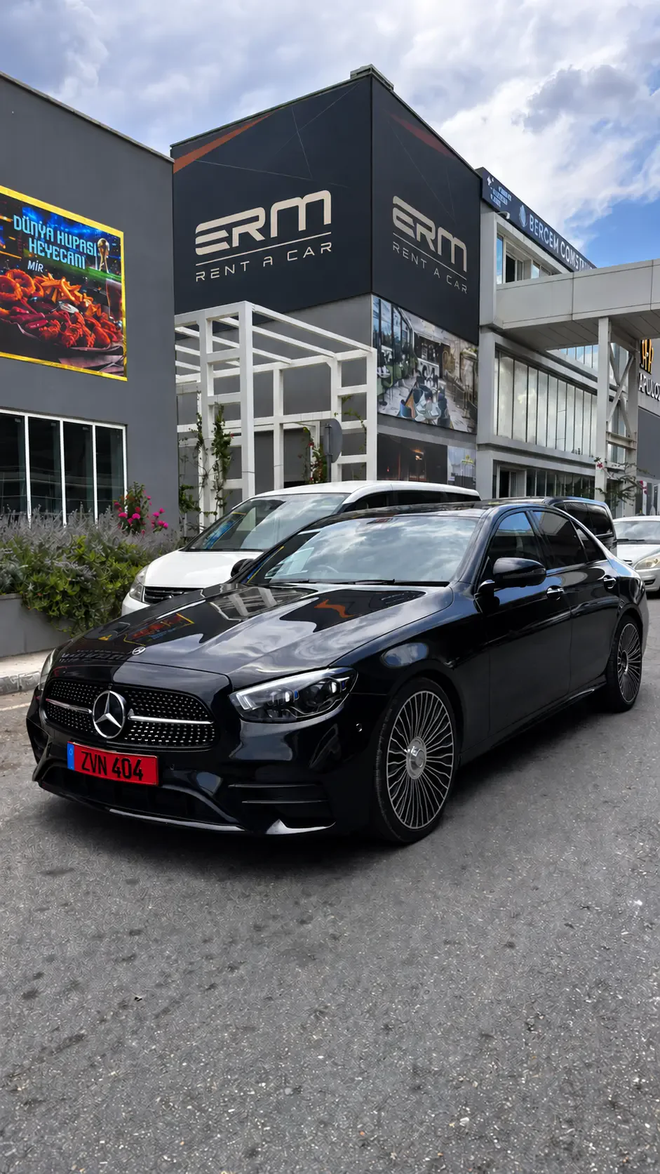 ERM Mercedes E 220 ön çapraz görünüm; arka plandaki tabela dijital olarak düzenlenmiştir
